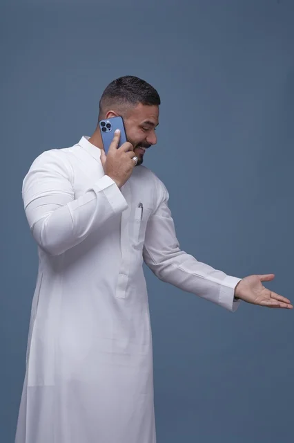 رجل سعودي يرتدي الثوب الأبيض يتحدث عبر الهاتف الذكي