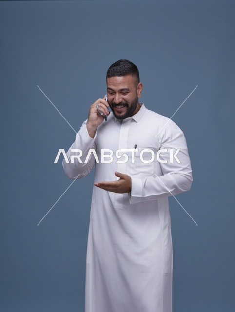 رجل سعودي بالثوب الأبيض يتحدث عبر الهاتف الذكي