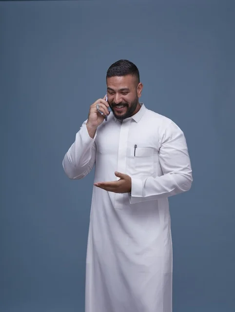 رجل سعودي بالثوب الأبيض يتحدث عبر الهاتف الذكي