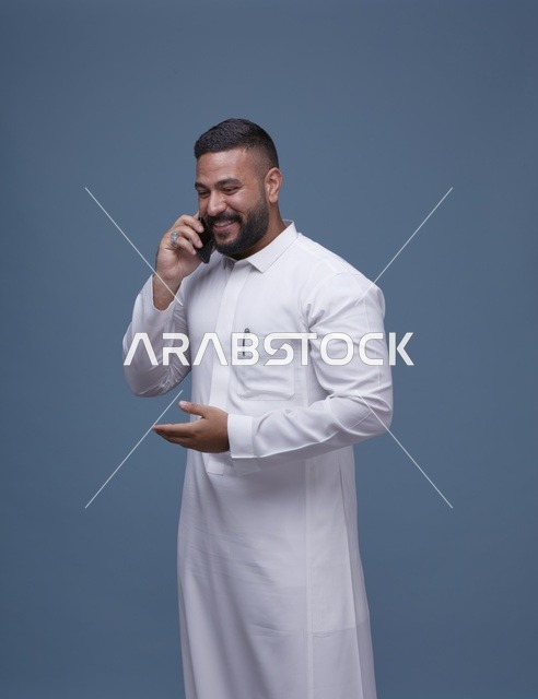 رجل سعودي بالثوب الأبيض يتحدث عبر الهاتف الذكي