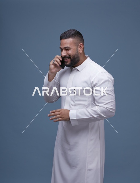 رجل سعودي بالثوب الأبيض يتحدث عبر الهاتف الذكي