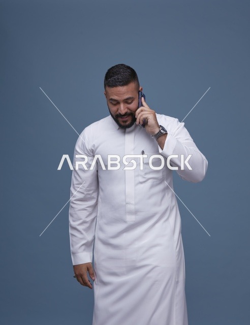 رجل سعودي بالثوب الأبيض يتحدث بالهاتف الذكي في استوديو