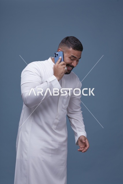 رجل سعودي بالثوب الأبيض يتحدث عبر الهاتف الذكي