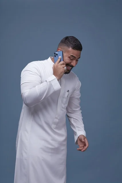 رجل سعودي بالثوب الأبيض يتحدث عبر الهاتف الذكي