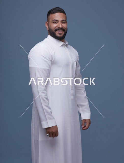 بورتريه لرجل سعودي مبتسم بالثوب الأبيض بخلفية زرقاء