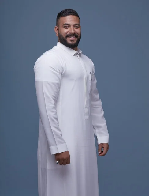 بورتريه لرجل سعودي مبتسم بالثوب الأبيض بخلفية زرقاء