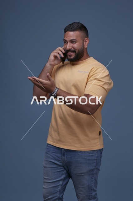 رجل سعودي مبتسم يتحدث بالهاتف في استوديو بخلفية زرقاء