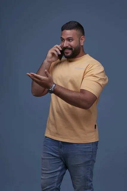 رجل سعودي مبتسم يتحدث بالهاتف في استوديو بخلفية زرقاء
