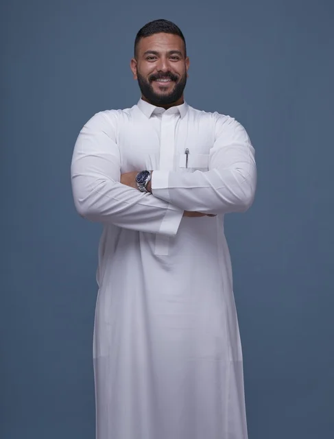 رجل سعودي مبتسم بالثوب الأبيض أمام خلفية زرقاء