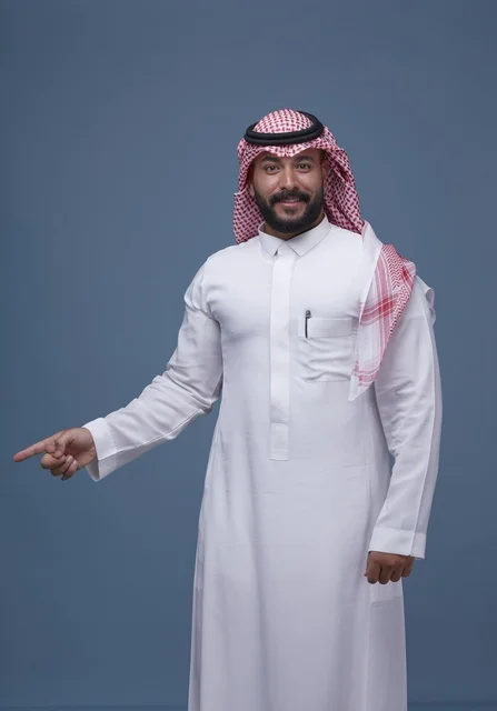 رجل سعودي بالثوب والشماغ يشير بيده بخلفية زرقاء