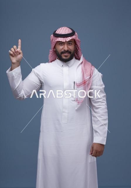 رجل سعودي بالثوب والشماغ التقليدي يشير بإصبعه للأعلى