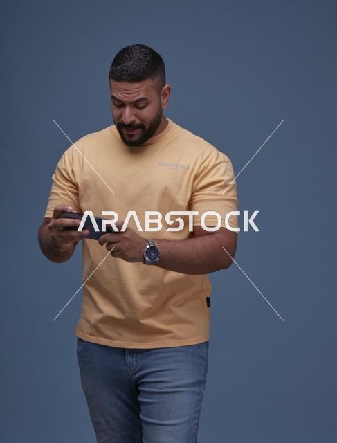شاب سعودي بملابس كاجوال يلعب على الهاتف الذكي في الاستوديو