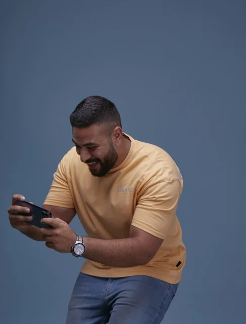 Saudi Man Playing Mobile Game on Smartphone in Casual Wear