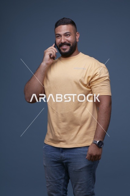رجل سعودي مبتسم يتحدث عبر الهاتف الذكي بملابس كاجوال