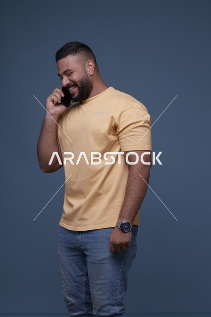 رجل سعودي مبتسم يتحدث بالهاتف بخلفية زرقاء