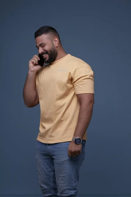 رجل سعودي مبتسم يتحدث بالهاتف بخلفية زرقاء