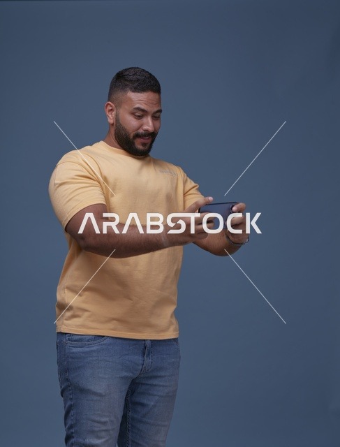 شاب سعودي بملابس كاجوال يلعب ألعاب الجوال بالاستوديو
