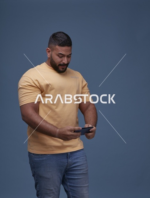 شاب سعودي بملابس كاجوال يلعب ألعاب الجوال في الاستوديو