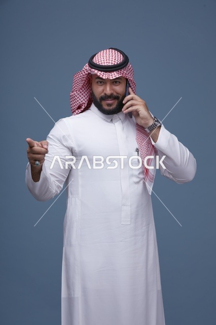 رجل سعودي مبتسم يتحدث بالجوال ويشير للأمام