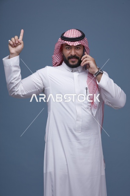 رجل سعودي مبتسم يتحدث بالهاتف الذكي ويشير بيده للأعلى