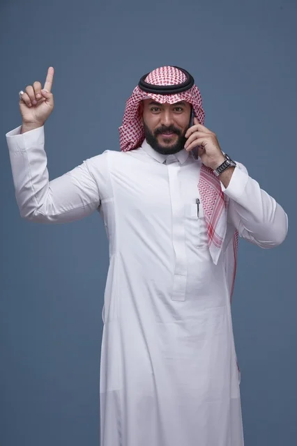 رجل سعودي مبتسم يتحدث بالهاتف الذكي ويشير بيده للأعلى