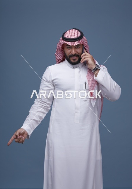 رجل سعودي يتحدث بالهاتف الذكي ويشير للأسفل في استوديو