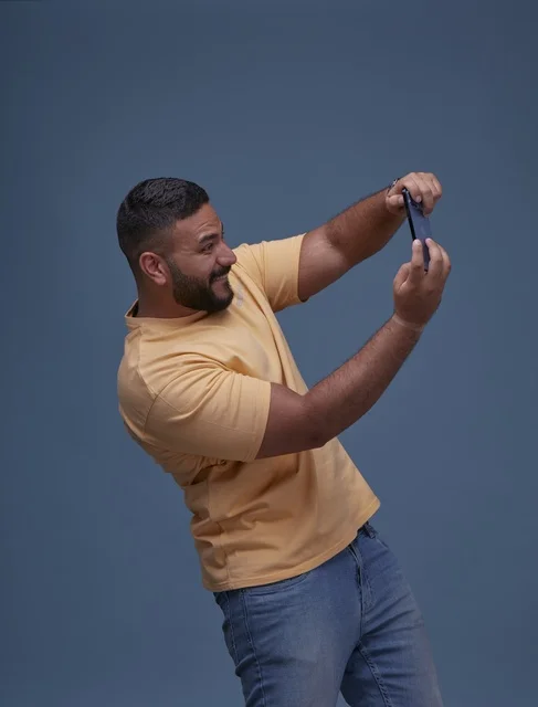شاب سعودي يلعب بهاتفه الذكي بملابس كاجوال