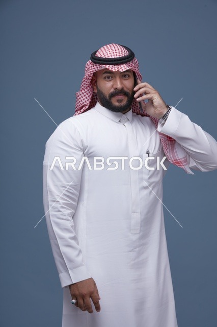 رجل سعودي مبتسم يتحدث عبر الهاتف الذكي في الاستوديو