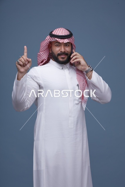 رجل سعودي مبتسم يتحدث بالهاتف الذكي ويشير للأعلى