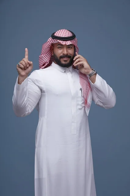 رجل سعودي مبتسم يتحدث بالهاتف الذكي ويشير للأعلى
