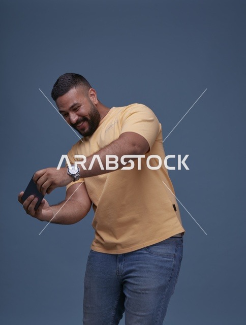 شاب سعودي يلعب بهاتفه الذكي في الاستوديو بملابس كاجوال