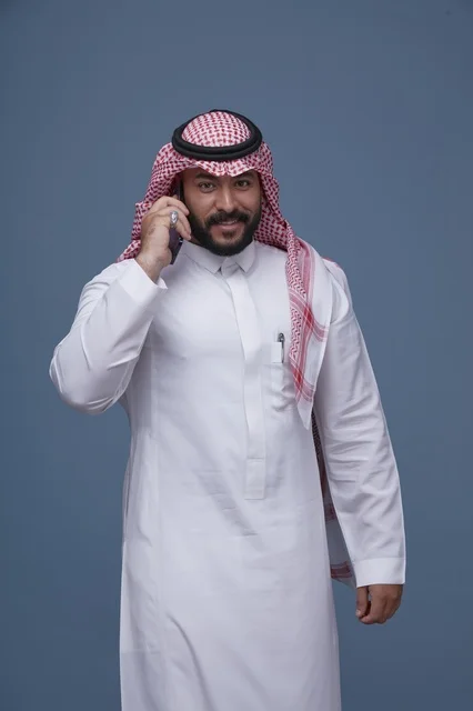 رجل سعودي مبتسم يتحدث عبر الهاتف الذكي بالزي التقليدي