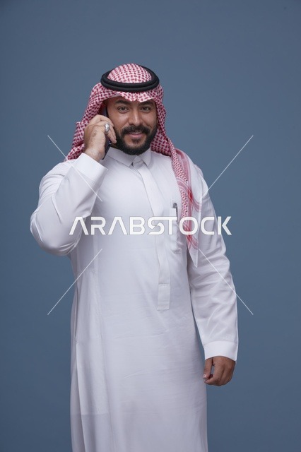 رجل سعودي مبتسم يتحدث عبر الهاتف الذكي في الاستوديو