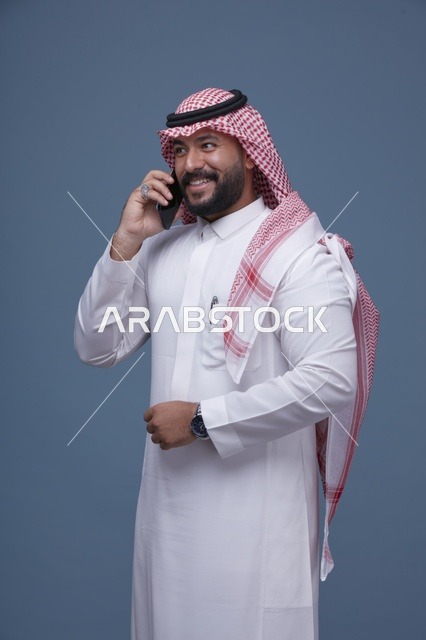 رجل سعودي مبتسم يتحدث بالهاتف الذكي في الاستوديو