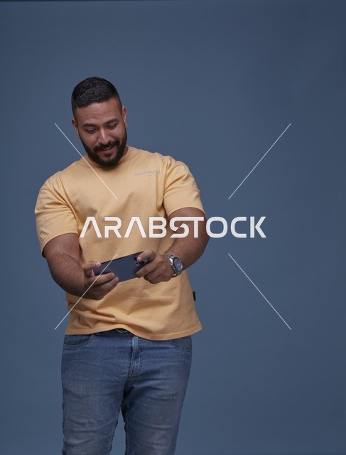شاب سعودي يلعب بهاتف ذكي أمام خلفية زرقاء سادة
