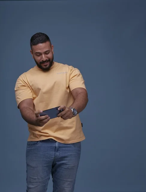 شاب سعودي يلعب بهاتف ذكي أمام خلفية زرقاء سادة