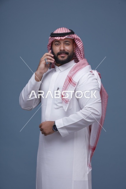 رجل سعودي مبتسم يتحدث بالجوال بالزي التقليدي