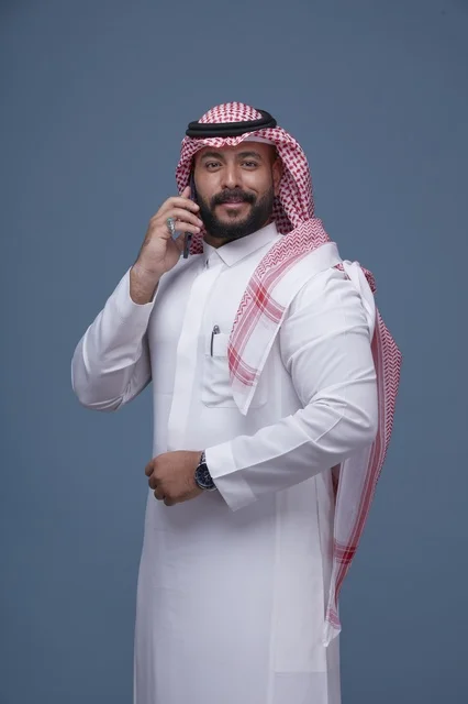 رجل سعودي مبتسم يتحدث بالجوال بالزي التقليدي