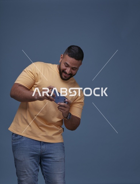 شاب سعودي يلعب بالهاتف الذكي بملابس كاجوال في الاستوديو
