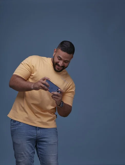 شاب سعودي يلعب بالهاتف الذكي بملابس كاجوال في الاستوديو