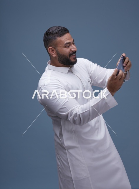 رجل سعودي بالثوب يستخدم الهاتف الذكي للألعاب