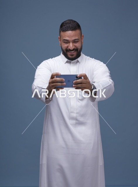 رجل سعودي بالثوب يلعب ألعاب المحمول بالهاتف الذكي