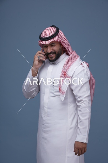رجل سعودي مبتسم يتحدث عبر الهاتف الذكي في الاستوديو