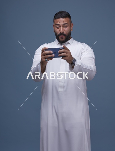 رجل سعودي يلعب بالهاتف الذكي بخلفية زرقاء