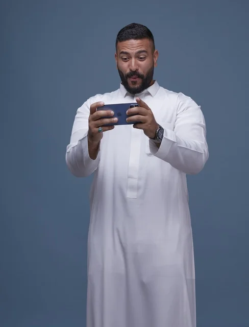 رجل سعودي يلعب بالهاتف الذكي بخلفية زرقاء