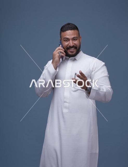 رجل سعودي بالثوب الأبيض يتحدث بالهاتف الذكي في استوديو