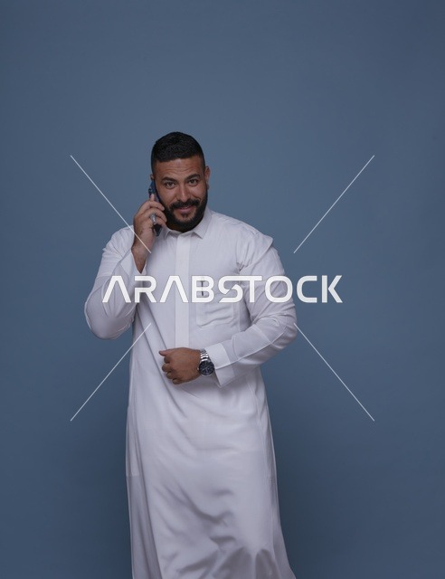 رجل سعودي بالثوب الأبيض يتحدث عبر الهاتف الذكي