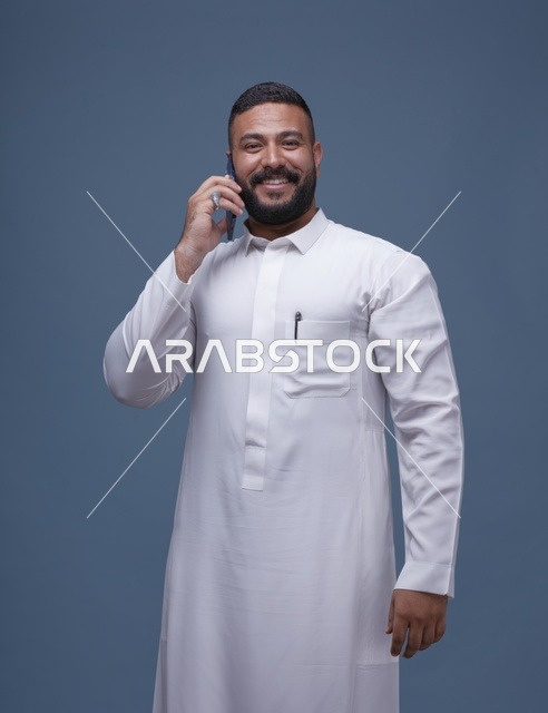 رجل سعودي بالثوب الأبيض يتحدث بالهاتف على خلفية زرقاء