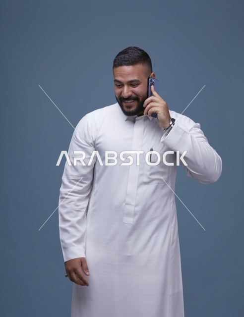 رجل سعودي بالثوب الأبيض يتحدث بالهاتف الذكي في استوديو