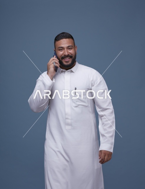 رجل سعودي يرتدي الثوب الأبيض يتحدث عبر الهاتف الذكي